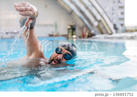 Focused swimmer performing crawl stroke in water. 136891752