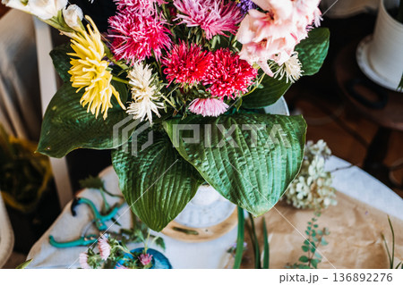Large colorful bouquet with yellow dahlia and pink asters sits in white stone urn. Botanical lifestyle, modern floral centerpieces, indoor nature, elegant floral accents. 136892276
