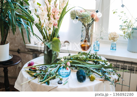 Floral arrangements and various tools sit on table in bright studio. Floral design techniques, flower pruning, professional florist tools, arrangement mechanics. 136892280