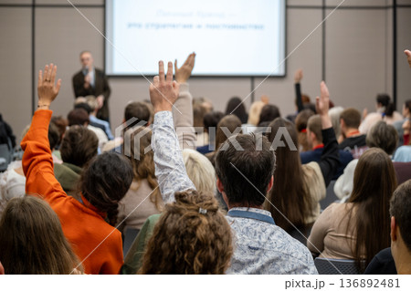 Audience at conference raising hands to ask questions during presentation in meeting room Audience at conference raising hands to ask questions during presentation in meeting room 136892481