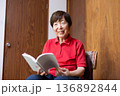 室内でイスに座って読書をするシニア女性 笑顔 正面 上半身 136892844