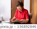 室内でイスに座って宅配サービスの注文をするシニア女性 ネットスーパー 136892846