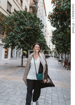 Woman Walking Confidently on City Street Lined with Orange Trees Woman Walking Confidently on City Street Lined with Orange Trees 136892891