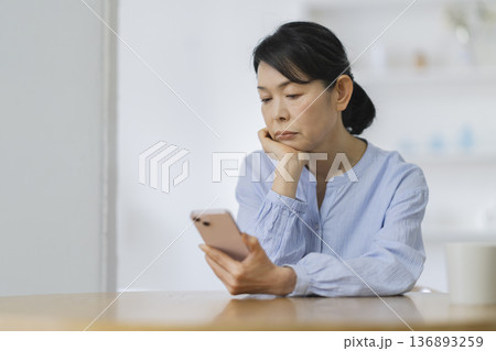 スマートフォンを見ながら考え込む50代後半の女性 136893259