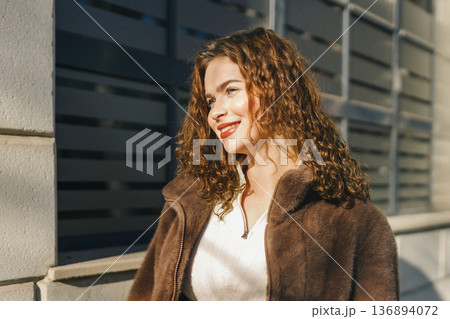 Young woman portrait near modern building facade in sunlight. Stylish casual outfit, soft shadows, confident look, contemporary urban lifestyle and fashion concept. Young woman portrait near modern building facade in sunlight. Stylish casual outfit, soft shadows, confident look, contemporary urban lifestyle and fashion concept. 136894072