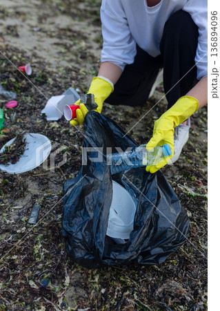 Volunteer collecting plastic waste during beach cleanup, removing litter and protecting the shoreline environment. Volunteer collecting plastic waste during beach cleanup, removing litter and protecting the shoreline environment. 136894096