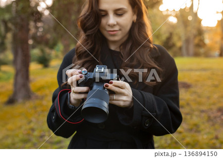 Close-up of a young woman holding a digital camera while photographing outdoors in warm sunlight. Soft golden-hour light, creative lifestyle photography moment. Close-up of a young woman holding a digital camera while photographing outdoors in warm sunlight. Soft golden-hour light, creative lifestyle photography moment. 136894150