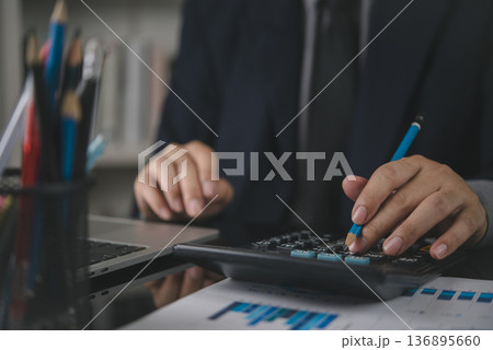 Accountant hand holding pencil use calculator. Business finance concept. Man working office desk, check financial report, data analysis graph, calculate budget, investment savings, paperwork. Accountant hand holding pencil use calculator. Business finance concept. Man working office desk, check financial report, data analysis graph, calculate budget, investment savings, paperwork. 136895660