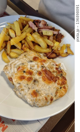 Grilled chicken fillet with cheese crust served with french fry and bacon on white plate. Concept of hearty lunch, comfort food and home style cuisine Grilled chicken fillet with cheese crust served with french fry and bacon on white plate. Concept of hearty lunch, comfort food and home style cuisine 136898091