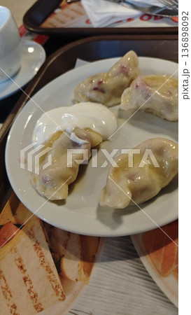 Boiled dumpling with sour cream served on white plate with cup of tea in cafe. Concept of traditional cuisine, comfort food and homemade meal 136898092