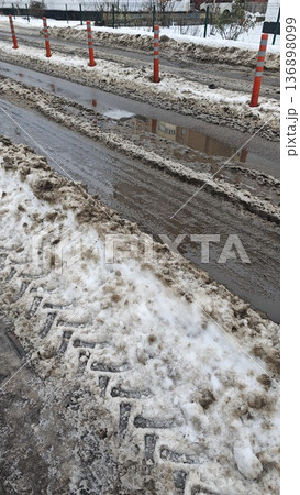 Dirty snow and slush on urban road with puddle and traffic bollard in winter day. Concept of seasonal weather, city infrastructure and hazardous driving condition 136898099