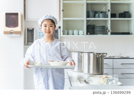 白衣を着てランチプレートを持つ給食当番の女の子 白衣を着てランチプレートを持つ給食当番の女の子 136899299