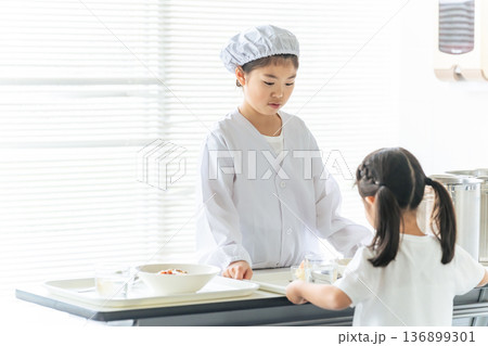 白衣を着て大鍋の料理を配膳する給食当番の女の子 白衣を着て大鍋の料理を配膳する給食当番の女の子 136899301