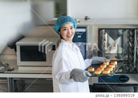 オーブンでパンを焼く衛生白衣を着た女性調理師　給食センター　給食室 136899319