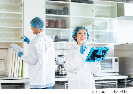 厨房をチェックする衛生白衣を着た男女作業員 136899360