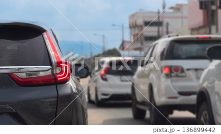 Rear side view of car with turn on brake light on the road. Traffic conditions on the road with many cars parked in a queue. Background blurred of city under blue sky. At Thailand. Rear side view of car with turn on brake light on the road. Traffic conditions on the road with many cars parked in a queue. Background blurred of city under blue sky. At Thailand. 136899442