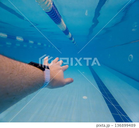 Underwater swimming pool lane with smartwatch and reaching hand Underwater swimming pool lane with smartwatch and reaching hand 136899489