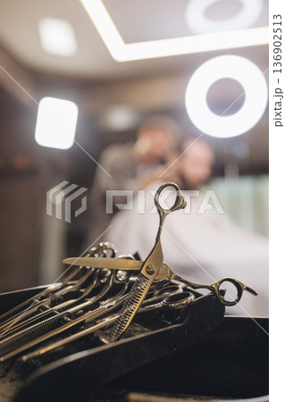 Professional barber scissors and grooming tools on workstation in modern barbershop. Close up of hairstyling equipment, selective focus, male grooming concept, salon atmosphere. Professional barber scissors and grooming tools on workstation in modern barbershop. Close up of hairstyling equipment, selective focus, male grooming concept, salon atmosphere. 136902513