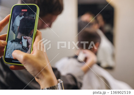 Smartphone recording barber haircut process in modern barbershop. Close up of mobile phone screen filming professional hair trimming, male grooming, content creation, social media concept. Smartphone recording barber haircut process in modern barbershop. Close up of mobile phone screen filming professional hair trimming, male grooming, content creation, social media concept. 136902519