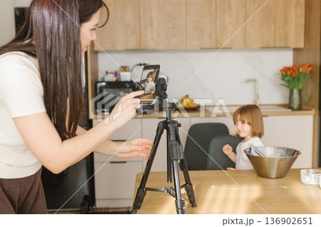 Mother recording daughter cooking on smartphone in kitchen, family creating home video content and baking together Mother recording daughter cooking on smartphone in kitchen, family creating home video content and baking together 136902651