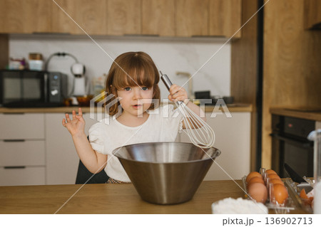 Little girl holding whisk over metal bowl in kitchen, child helping with baking at home, family lifestyle cooking scene Little girl holding whisk over metal bowl in kitchen, child helping with baking at home, family lifestyle cooking scene 136902713