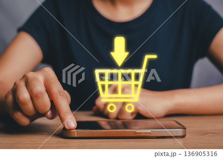 Close-up of a person using a smartphone with a glowing shopping cart icon, symbolizing online shopping and e-commerce. 136905316