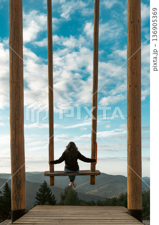 Woman Sitting on a Swing Over Mountain Valley 136905369