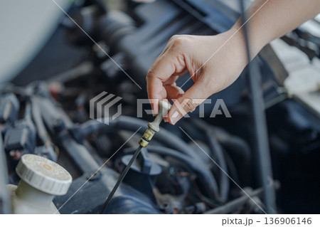 Close up of a  hand of woman pulling an engine oil dipstick to inspect oil level 136906146
