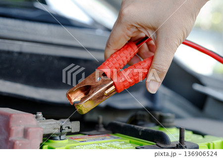 Hand holding jumper cable clamp near car battery Hand holding jumper cable clamp near car battery 136906524