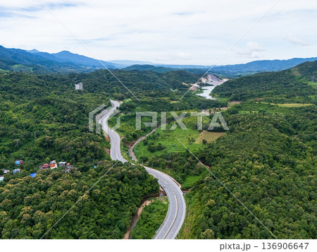 Aerial drone view of Highway 101 winding through lush green mountains between Phrae and Nan, Thailand. A scenic landscape of the road surrounded by tropical forest and a peaceful countryside 136906647