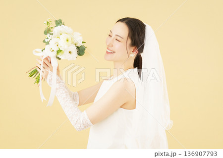 ベージュ背景のウェディングドレスを着てブーケを掲げる若い花嫁のポートレート 136907793