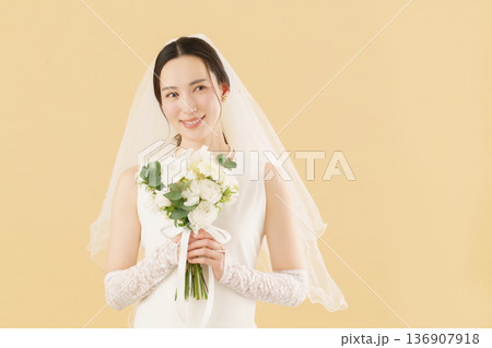 ベージュ背景のウェディングドレスを着る若い花嫁のポートレート ベージュ背景のウェディングドレスを着る若い花嫁のポートレート 136907918