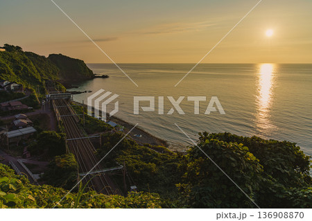夕暮れの日本海と青梅川駅を行くローカル線 136908870