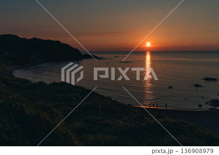 夕陽に染まる海辺と佇む人々のシルエット 136908979