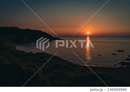夕陽に染まる海辺と佇む人々のシルエット 136908980
