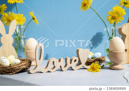 LOVE wooden word on festive blue background and eco-friendly zero waste natural decoration. Yellow daisies flowers. Bunny egg. Holiday greeting 136909999