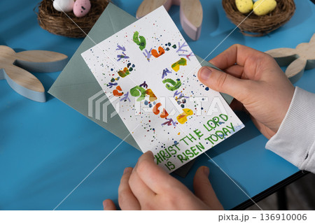 Person holding handmade greeting card with message CHRIST THE LORD IS RISEN TODAY written in beautiful handwriting. Gesture shows excitement and joy for the upcoming event. Springtime holiday gift Person holding handmade greeting card with message CHRIST THE LORD IS RISEN TODAY written in beautiful handwriting. Gesture shows excitement and joy for the upcoming event. Springtime holiday gift 136910006