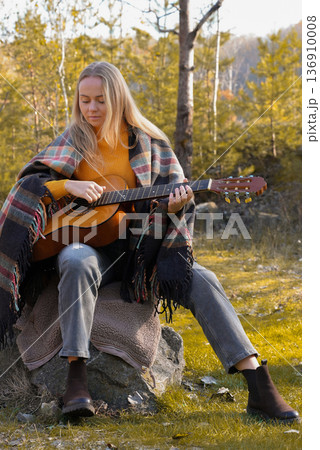 Portrait of smiling caucasian artist plays wooden acoustic guitar in autumnal park. Young songwriter plays string musical instrument hobby outside in nature fall time. Audio music healing 136910008