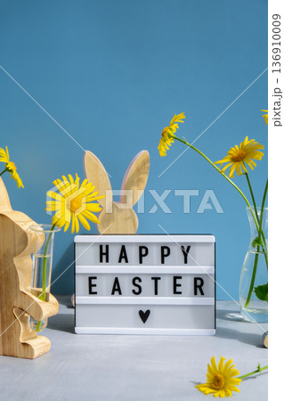 Happy Easter text on Lightbox with bunny wooden figures and fresh flowers. Easter composition content still life. Christian symbols Happy Easter text on Lightbox with bunny wooden figures and fresh flowers. Easter composition content still life. Christian symbols 136910009