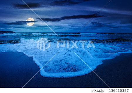 tide rolling on the sandy beach at night. full moon over sea waves beneath a cloudy sky. empty calm scenery in summer. loneliness concept. mysterious image for wallpaper or book cover use 136910327