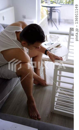 Future father assembling a white crib in a minimalist nursery ro Future father assembling a white crib in a minimalist nursery ro 136911149