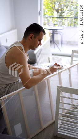 Future father assembling a white crib in a minimalist nursery ro Future father assembling a white crib in a minimalist nursery ro 136911150