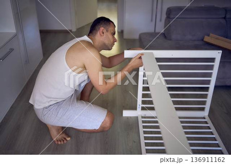 Expectant father preparing a nursery by assembling a wooden crib Expectant father preparing a nursery by assembling a wooden crib 136911162