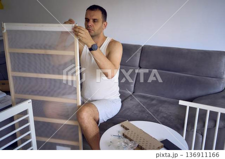 Future father assembling a white crib in a minimalist nursery room 136911166
