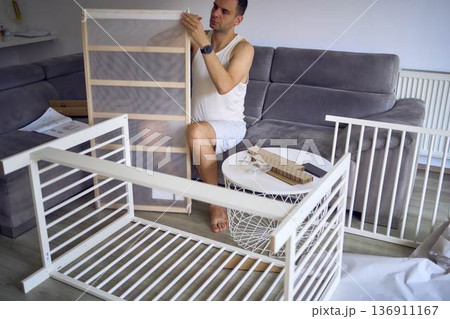 Future father assembling a white crib in a minimalist nursery room 136911167