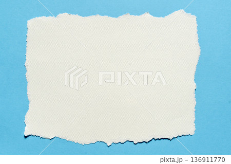 Torn piece of white textured paper on a blue background Torn piece of white textured paper on a blue background 136911770