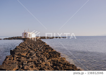 Coastal sentinel: the miniature stone church standing alone against the blue of the Mediterranean 136912046