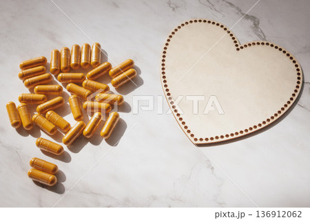 Heart-shaped wooden plate with scattered curcumin capsules on white marble, creating a warm, caring wellness scene, emphasizing natural health, love  136912062