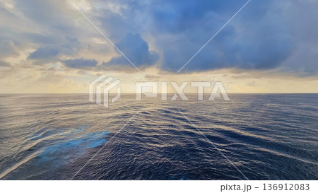 Vast pre-sunset ocean view with dark blue rippled water, dramatic layered cumulus clouds, golden sunlight at horizon, and foamy waves in foreground Vast pre-sunset ocean view with dark blue rippled water, dramatic layered cumulus clouds, golden sunlight at horizon, and foamy waves in foreground 136912083