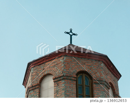 Brick church bell tower with metal cross on a clear spiritual sky. Religion and worship concept for architecture background. Brick church bell tower with metal cross on a clear spiritual sky. Religion and worship concept for architecture background. 136912653